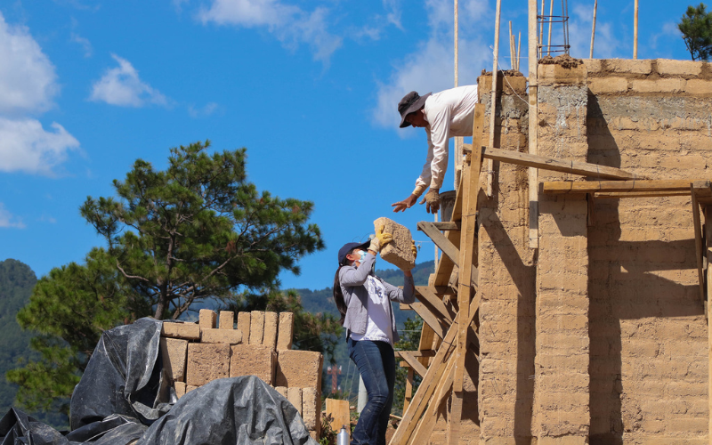 FUNDASAL Two People Passing Bricks